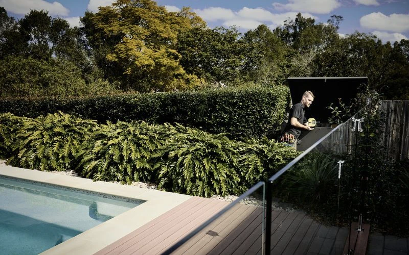 A man is standing on a railing next to a home pool.