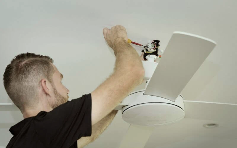 A man home fixing a ceiling fan.