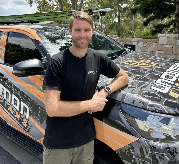 A man standing in front of a van with an orange and black wrap.