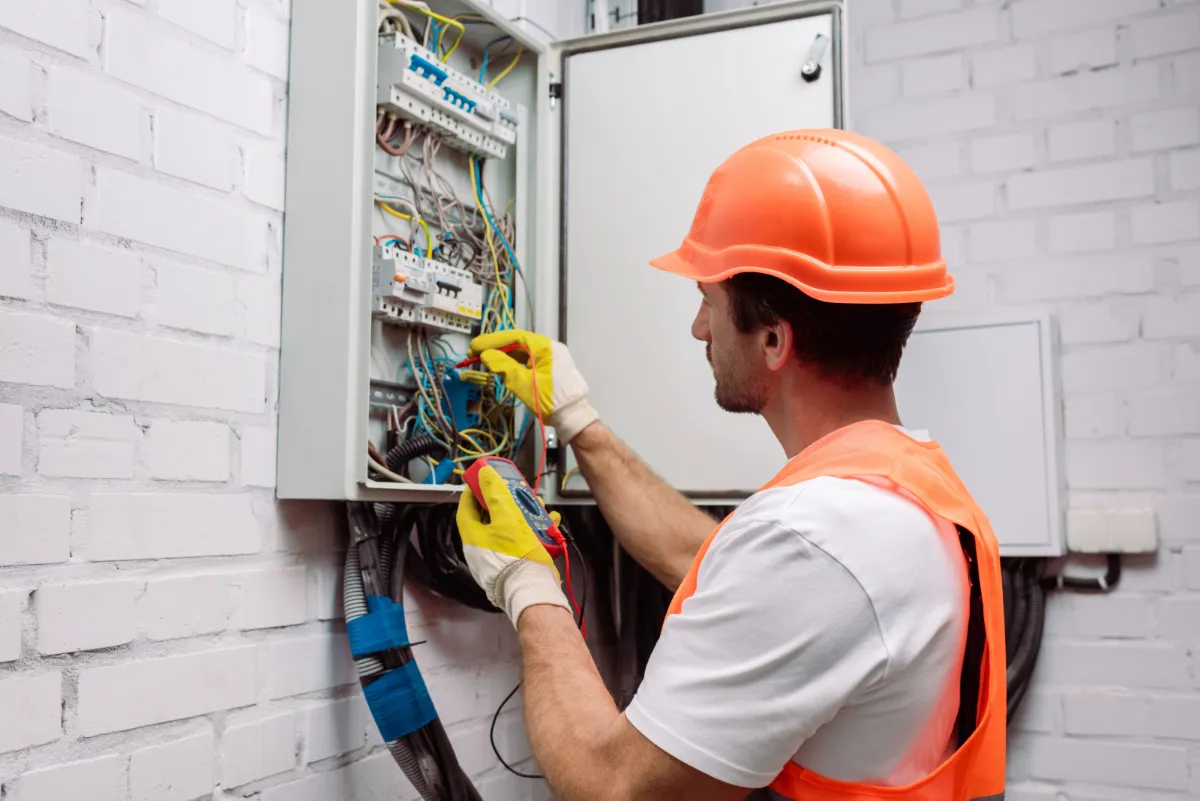 A man in an orange hard hat is working on an electrical panel as part of a shop fit-out project.